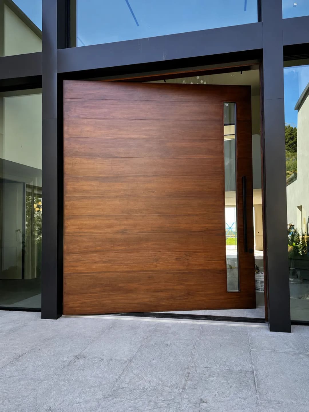 Large walnut-effect aluminium pivot door with a narrow glazed sidelight and a full-height glass surround