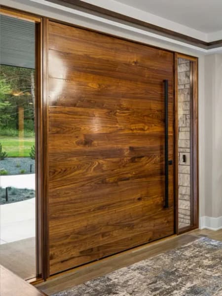 Warm walnut aluminium pivot door with a stone pilaster and recessed pull viewed from an interior