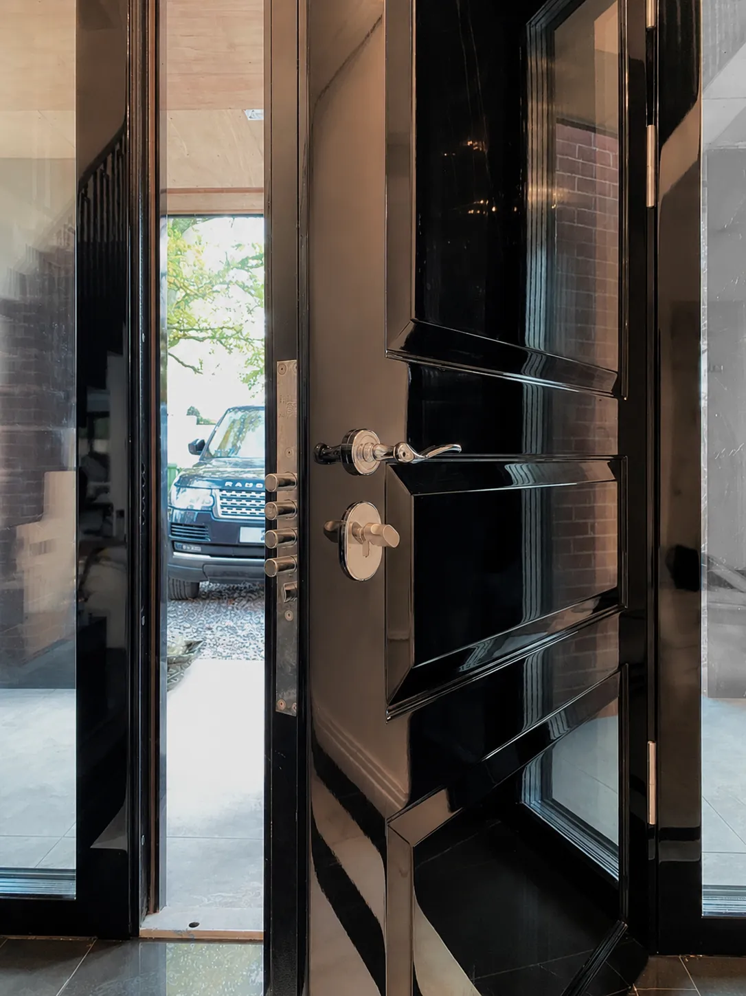 Black gloss security door open at an entrance with a chrome lever handle and multi-point bolts