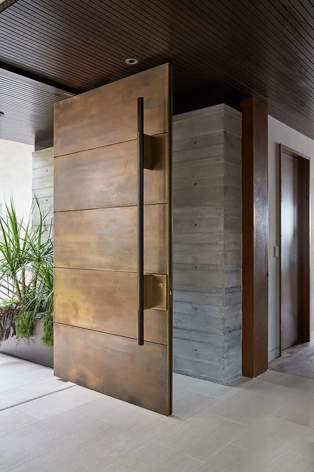 Aged-brass pivot door against a concrete interior