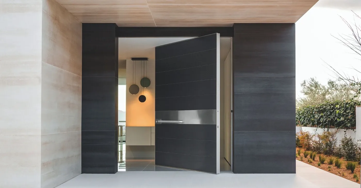 Patinated-bronze pivot door with a slim horizontal handle band beside a dark timber-slat feature wall
