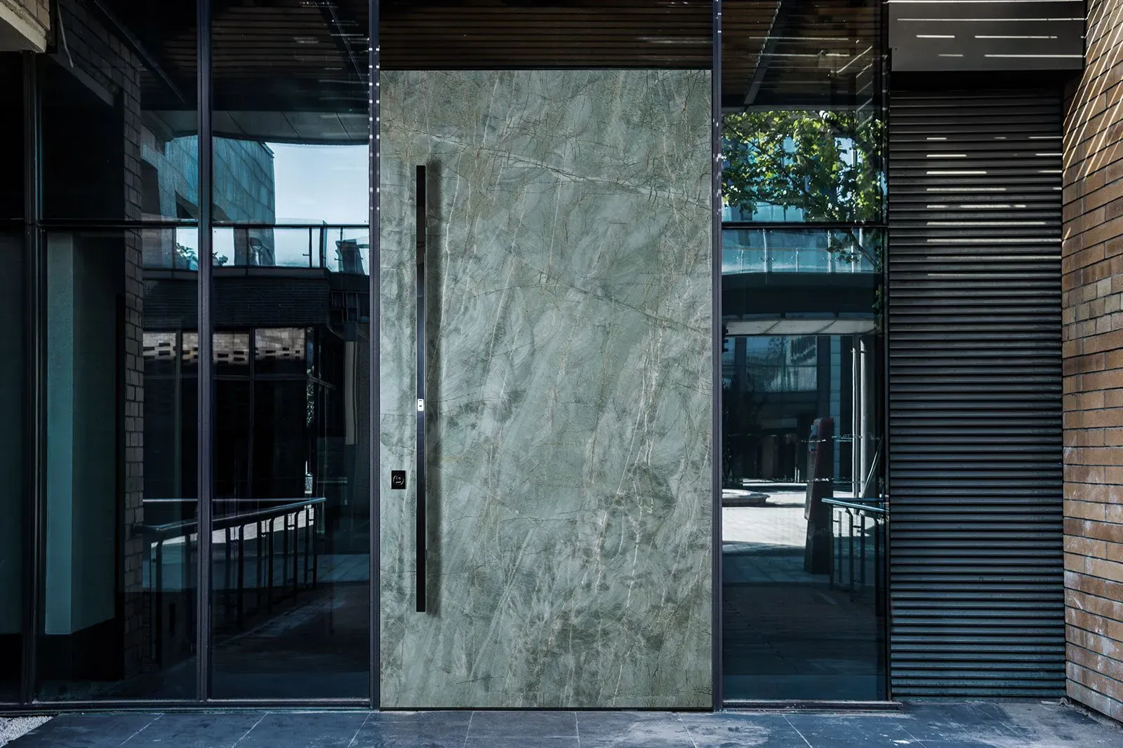 Green marble-effect aluminium pivot front door set in a glazed urban entrance