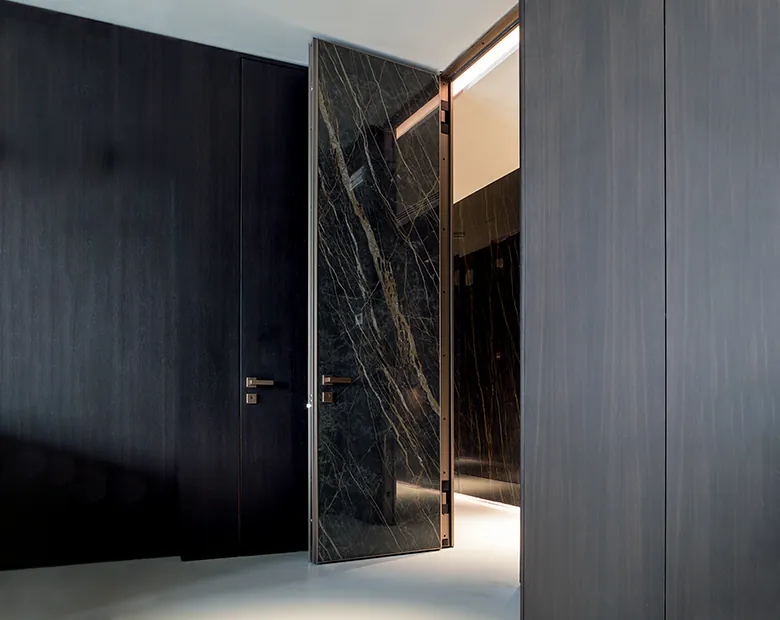 Black marble-effect aluminium pivot door ajar against a dark charcoal interior