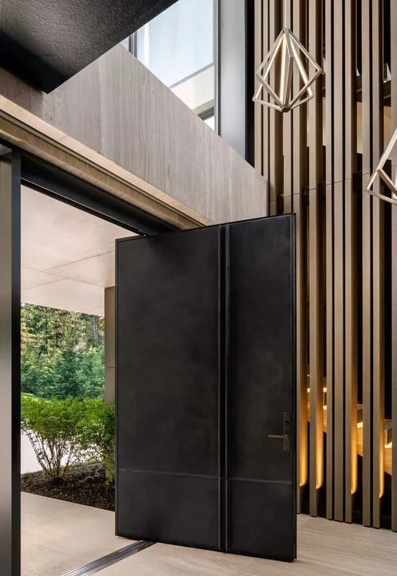 Matte-black pivot door in a timber-screen foyer with geometric pendant light