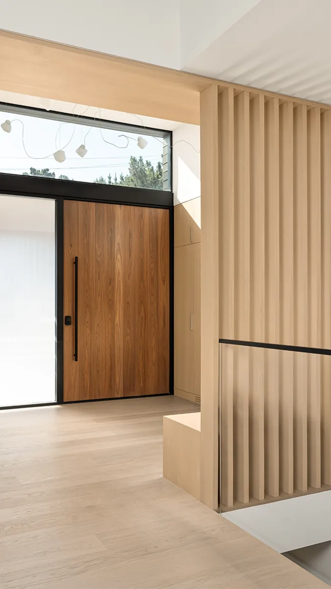 Walnut flush aluminium front door with sidelight viewed from a bright slatted hallway